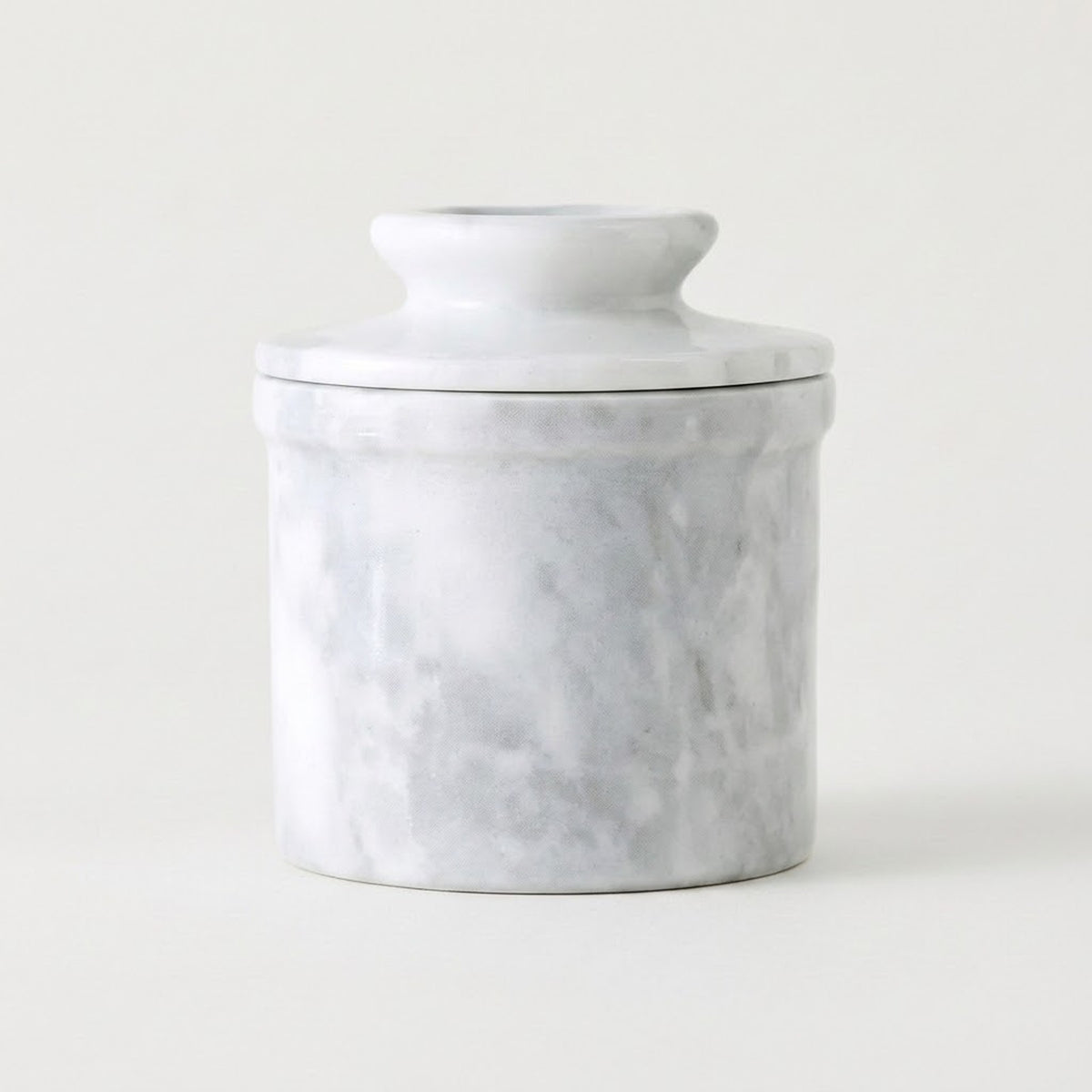 A small cylindrical lidded jar or container with a white marble-look surface and soft gray veining, photographed on a clean white background.