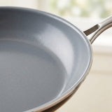 Close-up of a gray non-stick frying pan with a metallic silver handle, shown against a softly blurred light background.