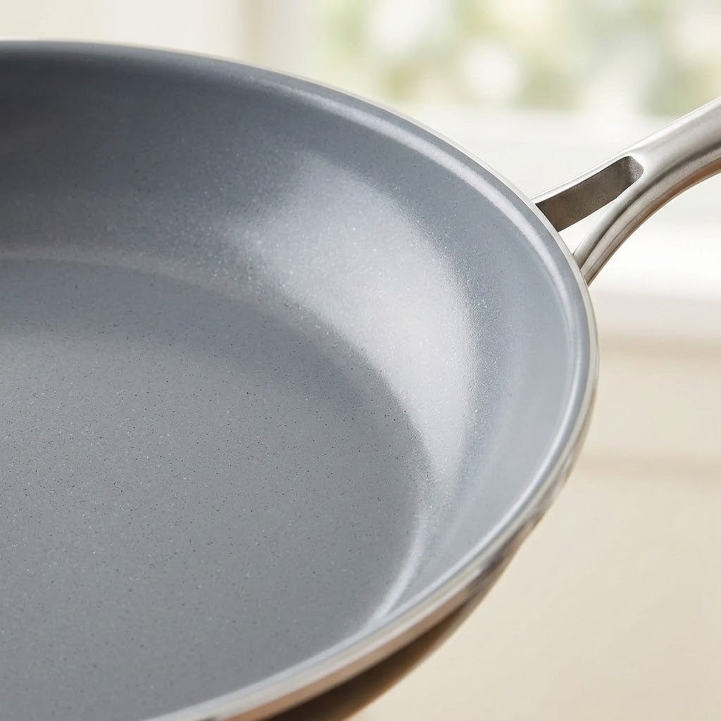 Close-up of a gray non-stick frying pan with a metallic silver handle, shown against a softly blurred light background.
