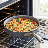 A gray nonstick skillet with a stainless steel handle sits on an oven rack inside an oven, holding a cooked breakfast pie or frittata with broccoli, red peppers, and mushrooms.