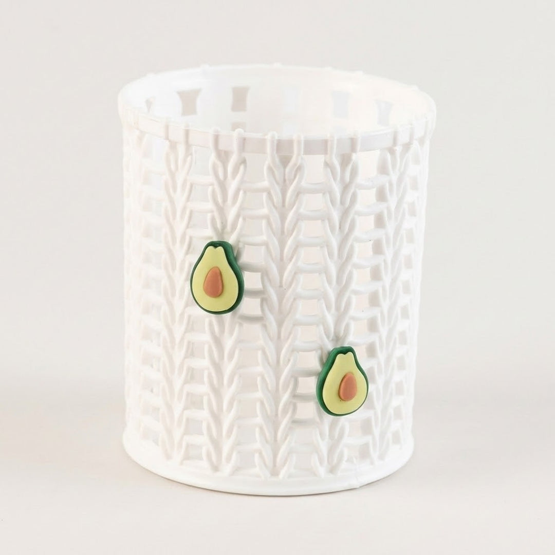 A white cylindrical storage basket with a textured basketweave pattern, featuring two small avocado-shaped decorative accents on the front, set against a plain light background.
