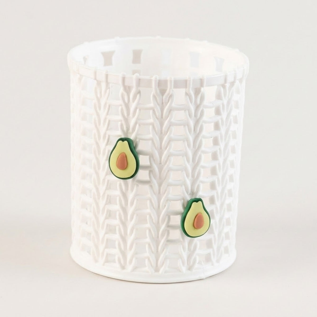 A white cylindrical storage basket with a textured basketweave pattern, featuring two small avocado-shaped decorative accents on the front, set against a plain light background.