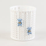 A white cylindrical plastic organizer or basket with a textured basketweave pattern, featuring two small blue teddy bear charms wearing yellow bowties attached to the front.