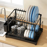 A black plastic and wire dish rack on a wooden kitchen countertop next to a sink, holding several blue and white plates and clear drinking glasses.