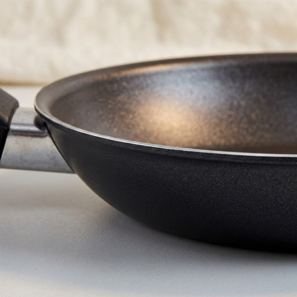 Close-up of a black non-stick frying pan with a metallic silver handle, resting on a light gray surface.