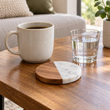 Round acacia wood and marble coaster sits beside a ceramic mug and drinking glass for scale.