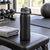 Black 24 oz insulated straw bottle rests beside a towel on a gym bench after a workout.