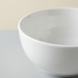 A close-up of a white ceramic bowl with a smooth, matte finish, set against a neutral light gray and beige background.