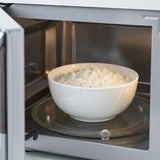 A white ceramic bowl filled with white rice sits on a glass turntable inside an open silver microwave oven.