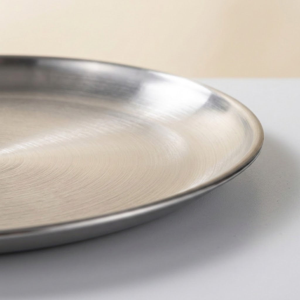 A close-up of a brushed stainless steel round tray or plate, showing its metallic texture and curved rim against a neutral light background.