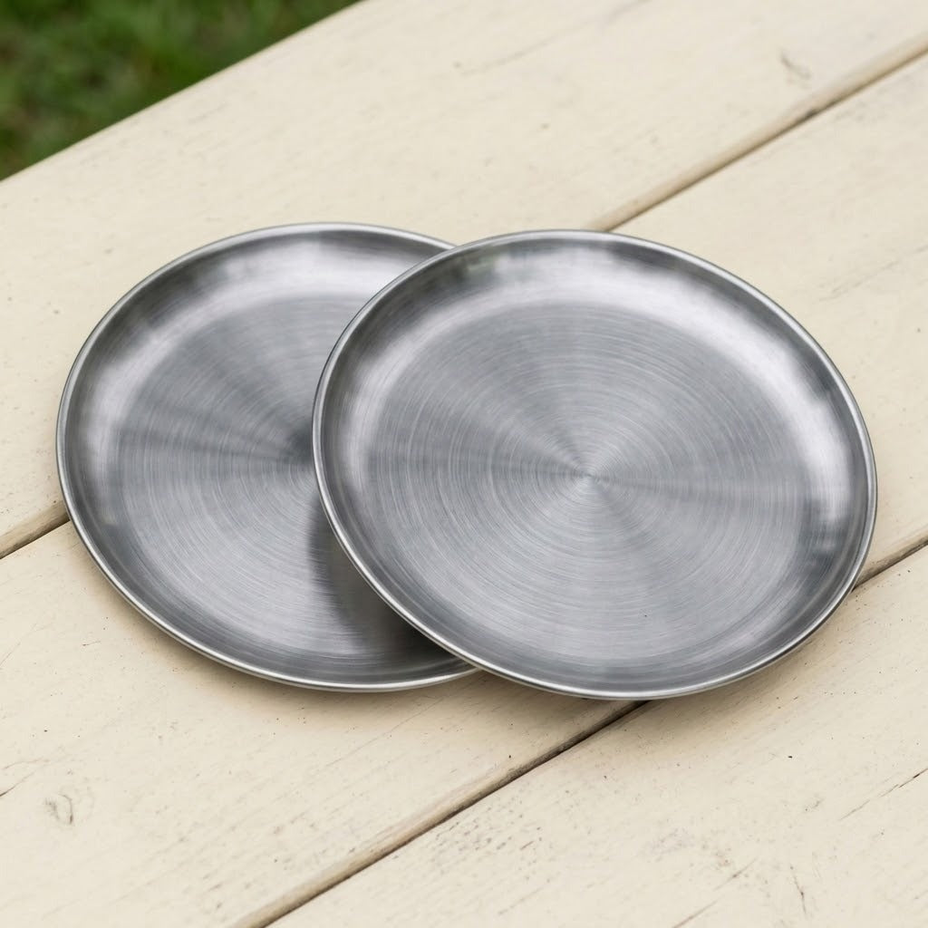 Two round brushed metal trays or shallow plates overlapping on a light wood surface outdoors.