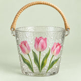 Tulip floral hammered glass ice bucket with woven handle on a pale green backdrop.