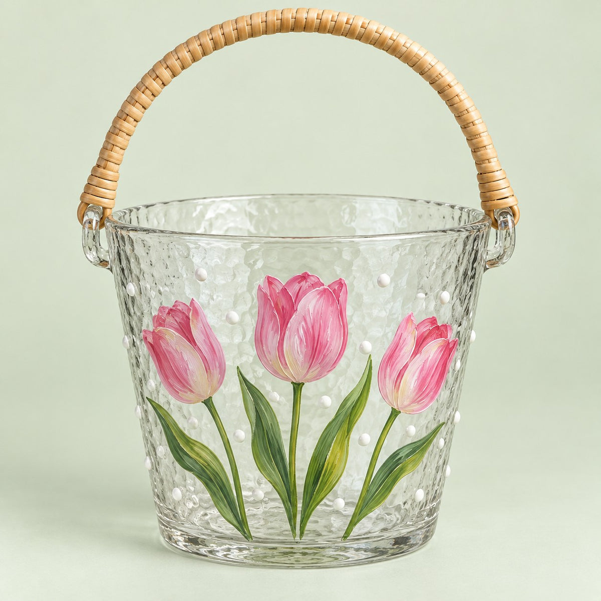 Tulip floral hammered glass ice bucket with woven handle on a pale green backdrop.