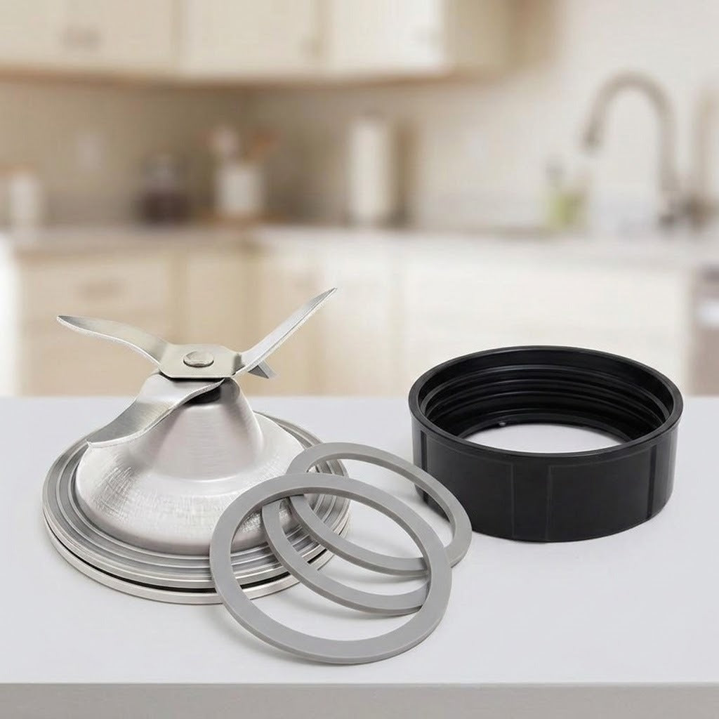 A metal blender blade assembly with a silver blade, silver collar, and two gray rubber seals, shown next to a black plastic jar lid rim on a white countertop with a blurred kitchen background.