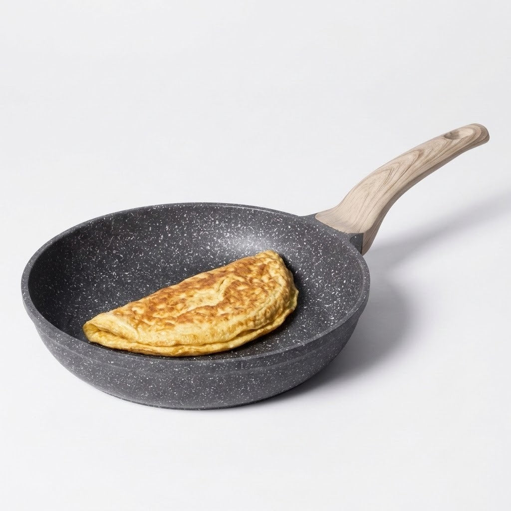 A dark gray speckled non-stick frying pan with a light wood handle, containing a folded golden-brown pancake or crepe, set against a plain light gray background.