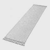 A long, narrow white fabric runner with a subtle tonal floral pattern and tassel fringe on both ends, shown on a light gray background.