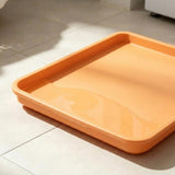 An orange rectangular plastic tray with raised edges, shown on a light beige tiled floor with soft natural shadows.