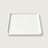 A minimalist square white tray with a slightly raised rim, photographed from a top-down angle on a light beige background.