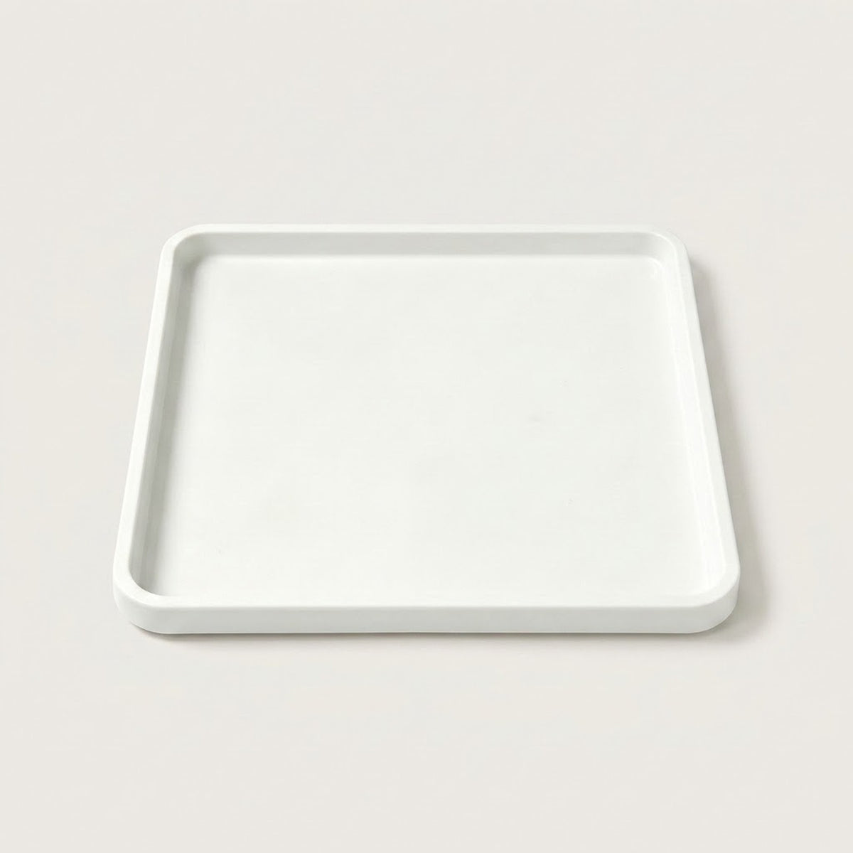 A minimalist square white tray with a slightly raised rim, photographed from a top-down angle on a light beige background.