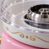 Close-up of the cotton candy maker's clear dome, polished metal spinner, white bowl, and gold trim.