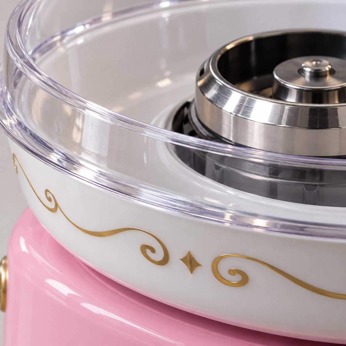 Close-up of the cotton candy maker's clear dome, polished metal spinner, white bowl, and gold trim.