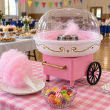 Pink cotton candy maker beside hard candies and a finished cone at a festive fundraising table.