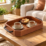 Rectangular wooden serving tray carries tea cups and biscuits together across a warm living room.