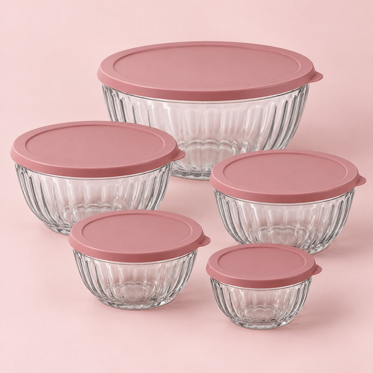 Five clear fluted glass mixing bowls with rose lids centered on a soft pink backdrop.