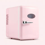 A retro-style mini refrigerator in pastel pink with a silver handle and oval window, shown on a light pink background.