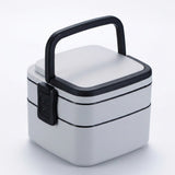 A square-shaped stainless steel lunch box with a black handle and black trim, shown on a clean white background.