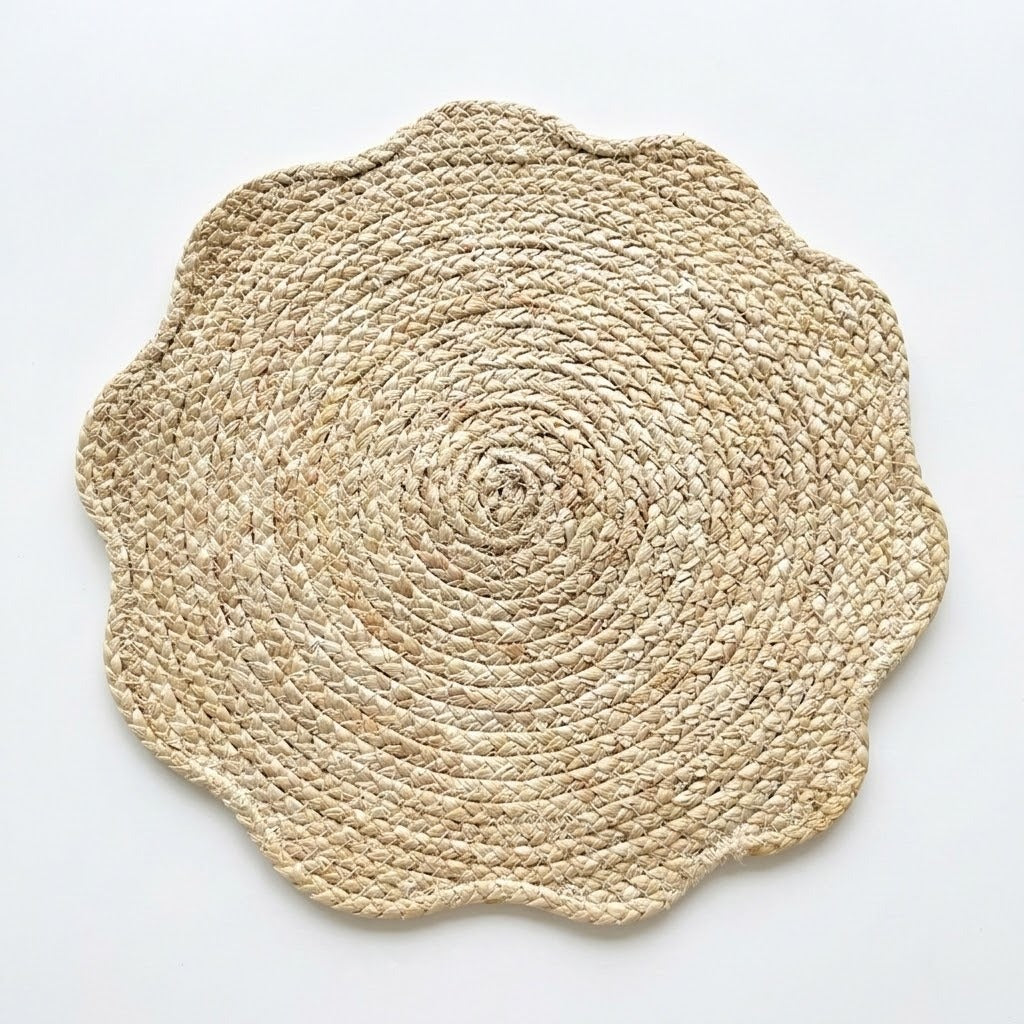 A round woven placemat with a scalloped edge, made from natural jute or seagrass fibers, shown on a plain white background.