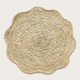 A round natural jute placemat with a scalloped edge, photographed from directly above on a light beige background.