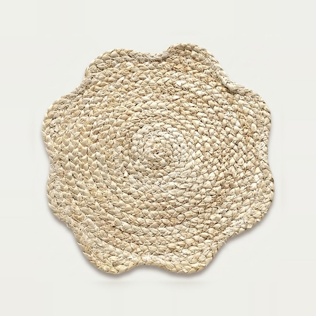 A round woven seagrass placemat with a scalloped edge, shown from a top-down view on a light off-white background.
