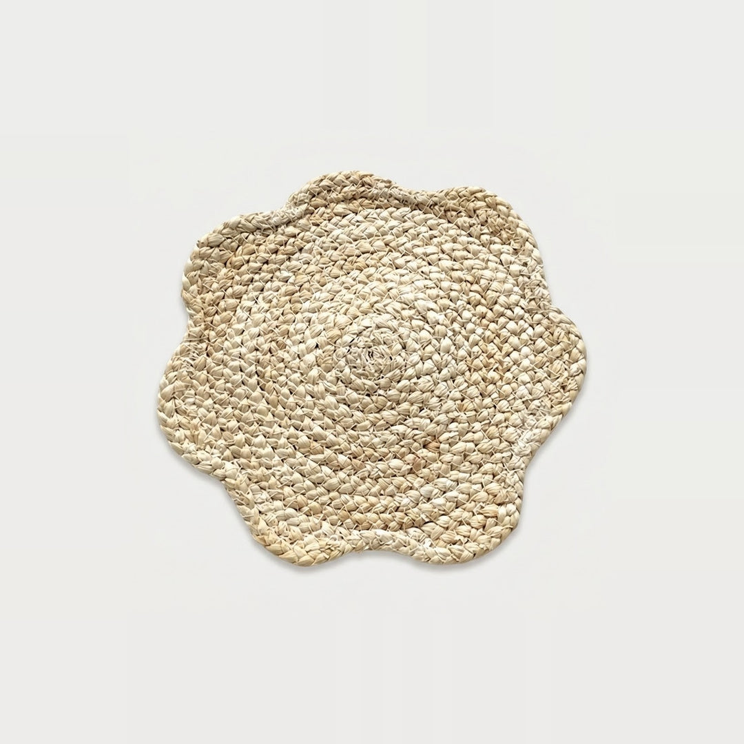 A round woven seagrass placemat with a scalloped edge, shown from a top-down view on a light gray background.