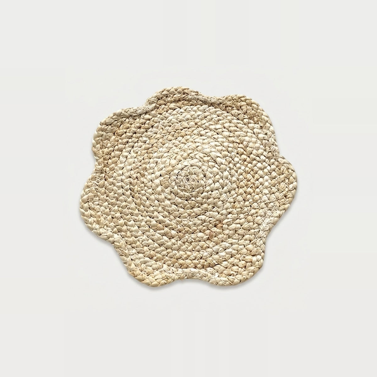 A round woven seagrass placemat with a scalloped edge, shown from a top-down view on a light gray background.