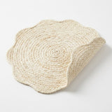 A round braided jute placemat with a scalloped edge, shown on a clean white background with one corner folded over to reveal the underside.