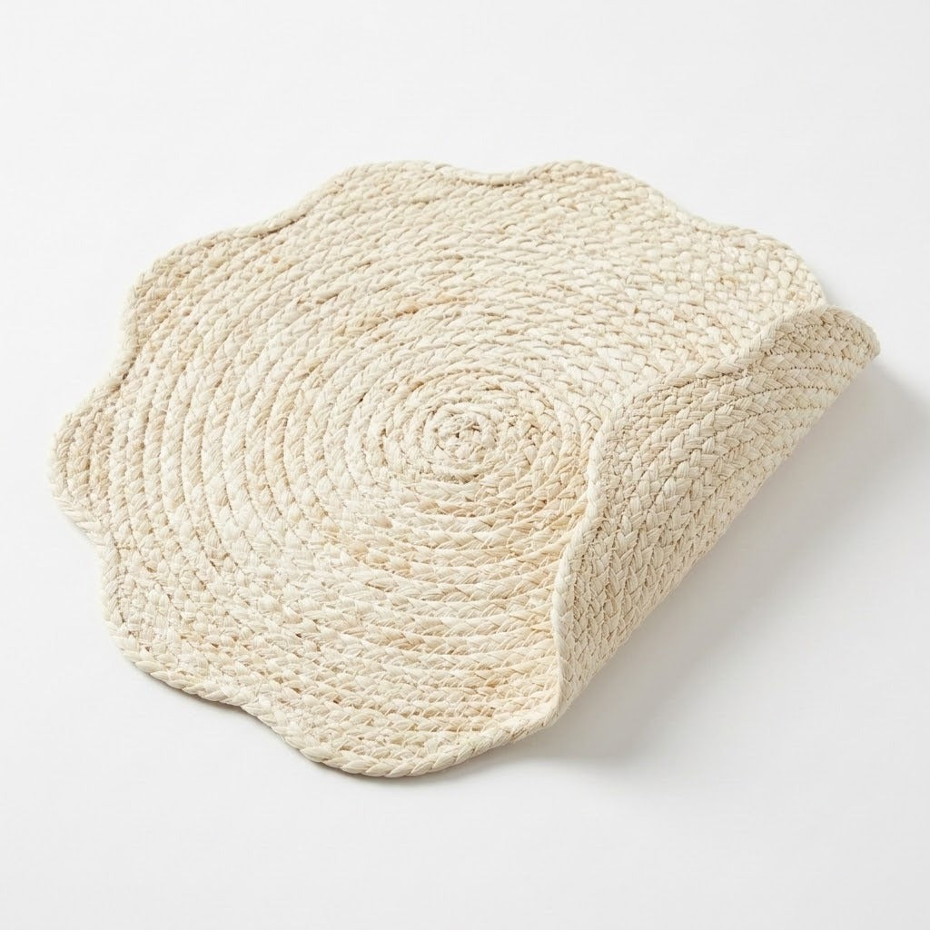 A round braided jute placemat with a scalloped edge, shown on a clean white background with one corner folded over to reveal the underside.