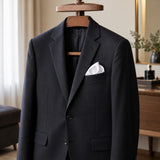 A plain white polyester pocket square adds a neat finishing detail to a dark suit jacket in a dressing room.