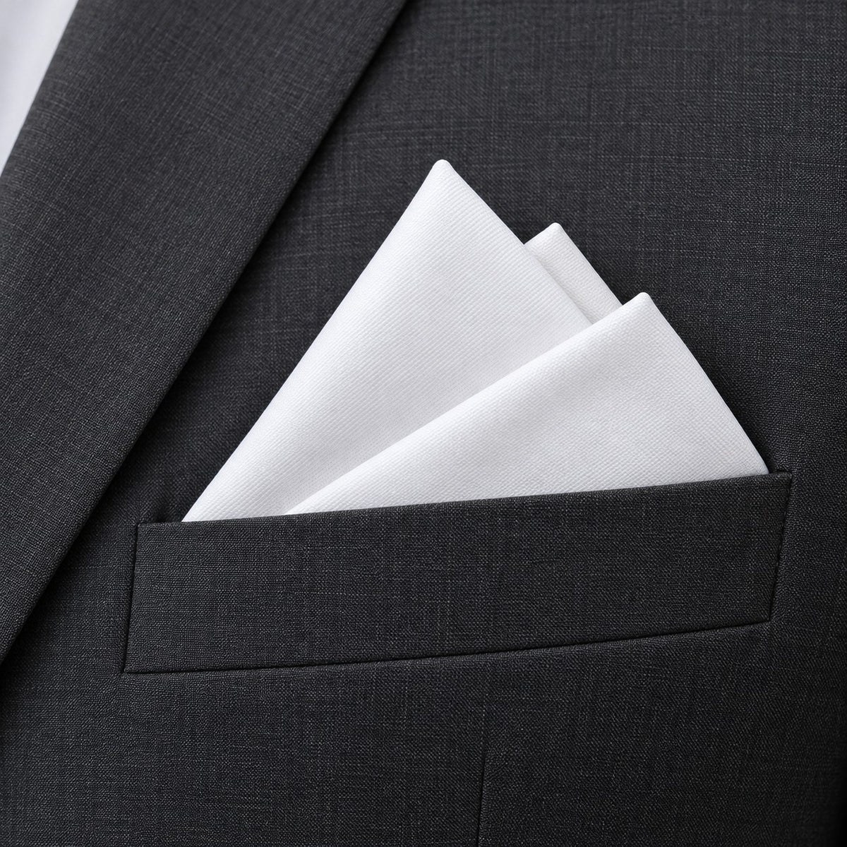 A crisp white polyester pocket square sits in a layered fold on a charcoal suit, showing its clean solid color.