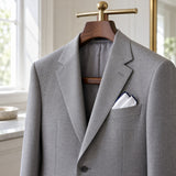 A white pocket square with navy edging finishes the breast pocket of a light gray suit jacket.