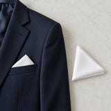 A folded white polyester pocket square rests beside a suit jacket pocket to show its compact scale.