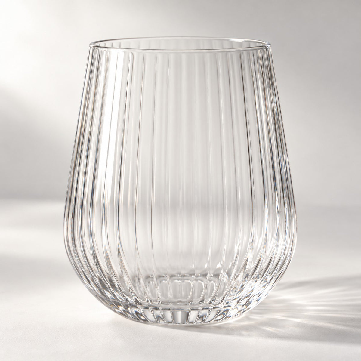 Clear ribbed stemless plastic wine glass highlights its textured sides on a bright studio backdrop.