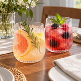 Ribbed stemless plastic wine glasses display citrus and berry cocktails on a home dining table.