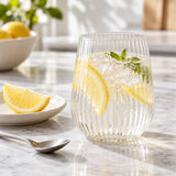 Clear ribbed stemless plastic wine glass beside a lemon wedge and teaspoon on a kitchen table.