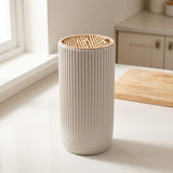 A ribbed ceramic tooth holder with a natural bamboo lid sits on a light countertop in a bright kitchen setting.