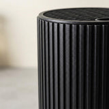 Close-up of a black ribbed cylindrical product, showing a slotted top surface against a softly blurred light background.