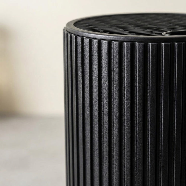 Close-up of a black ribbed cylindrical product, showing a slotted top surface against a softly blurred light background.