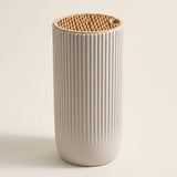 A ribbed ceramic tumbler in a warm off-white color with a natural light wood lid, photographed on a solid light beige background.