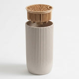 A ribbed ceramic cup in a warm off-white color with a matching bamboo lid featuring silicone bristles, set against a plain white background.