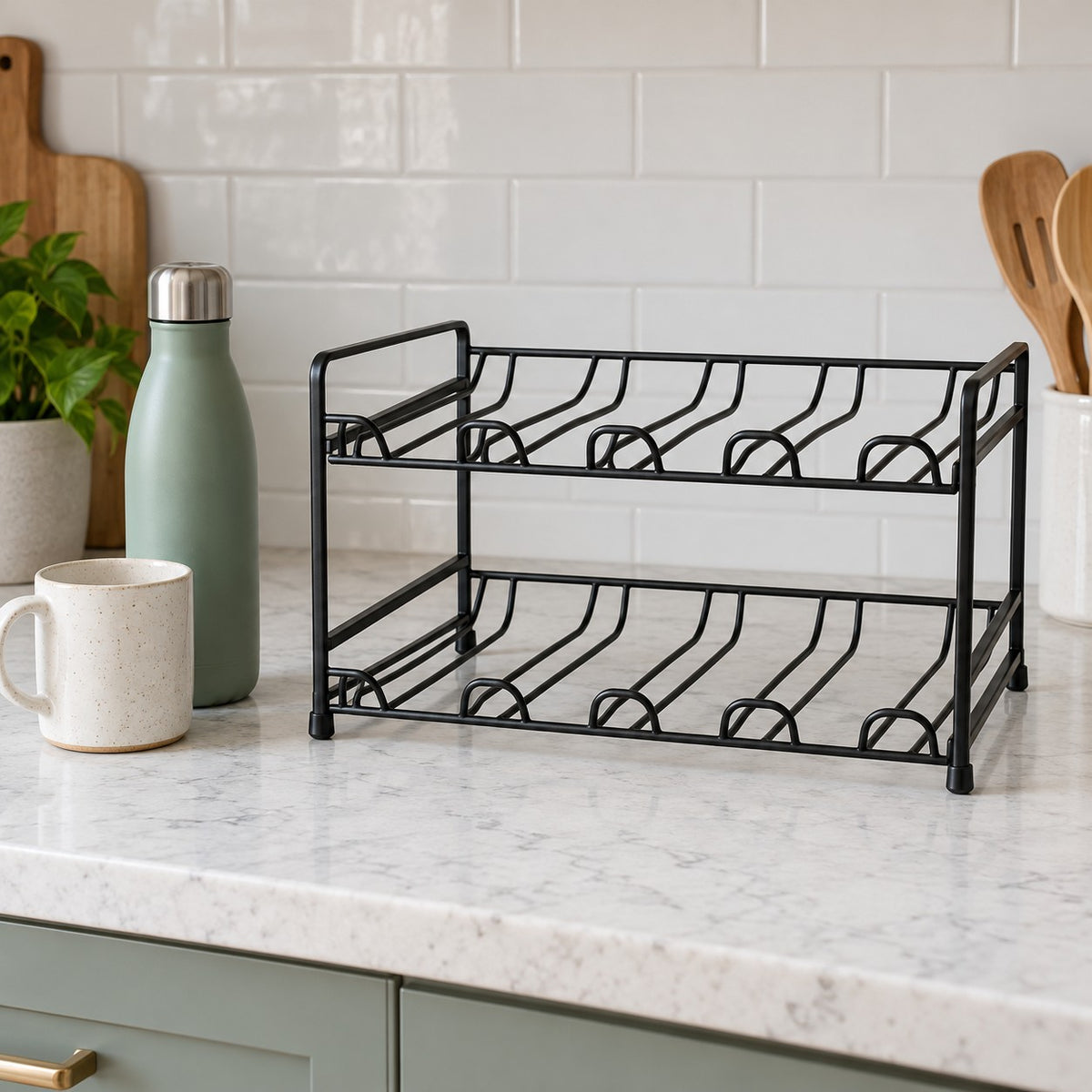 Black two-tier water bottle organizer sits beside a mug and bottle to show its compact kitchen scale.